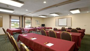 Une salle de conférence équipée de tables et de chaises, d’un écran de projection et d’une fenêtre donnant sur un espace verdoyant.