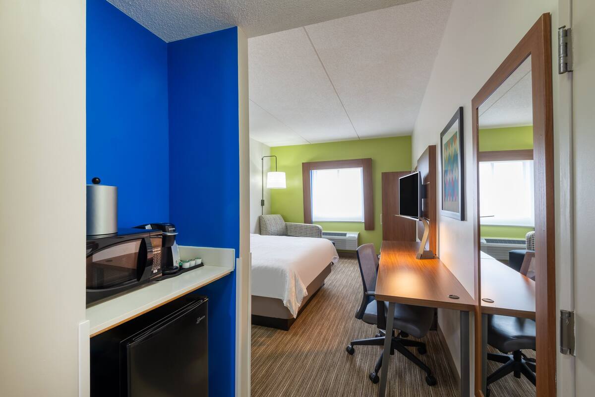 A hotel room with a bed, desk, chair, microwave, and TV.