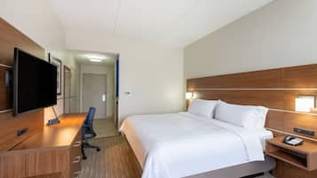 Quarto de hotel com uma cama, uma mesa com computador, televisão e telefone.