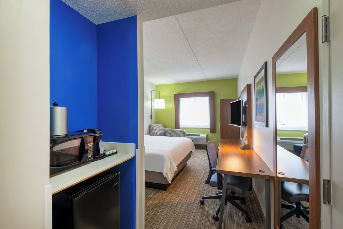 Une chambre d’hôtel équipée d’un lit, d’un bureau, d’une chaise, d’un micro-ondes et d’une télévision.