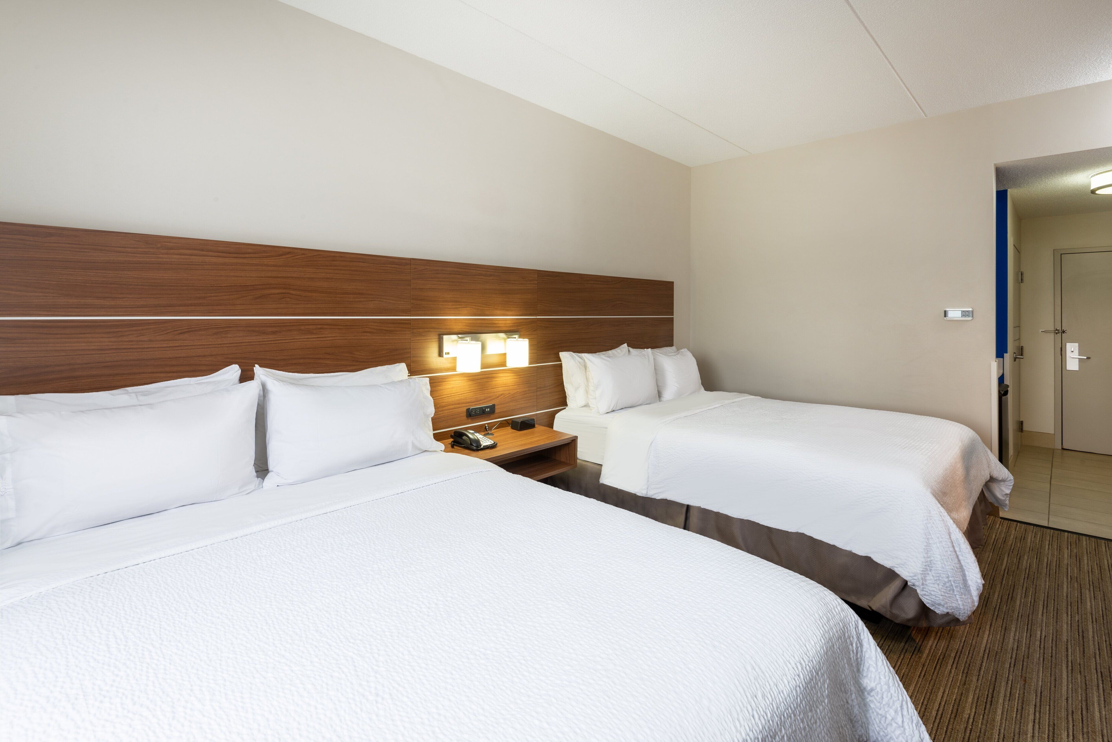 Ein Hotelzimmer mit zwei Betten, einem Holzkopfteil, Nachttischlampen und einem kleinen Tisch mit einem Telefon.