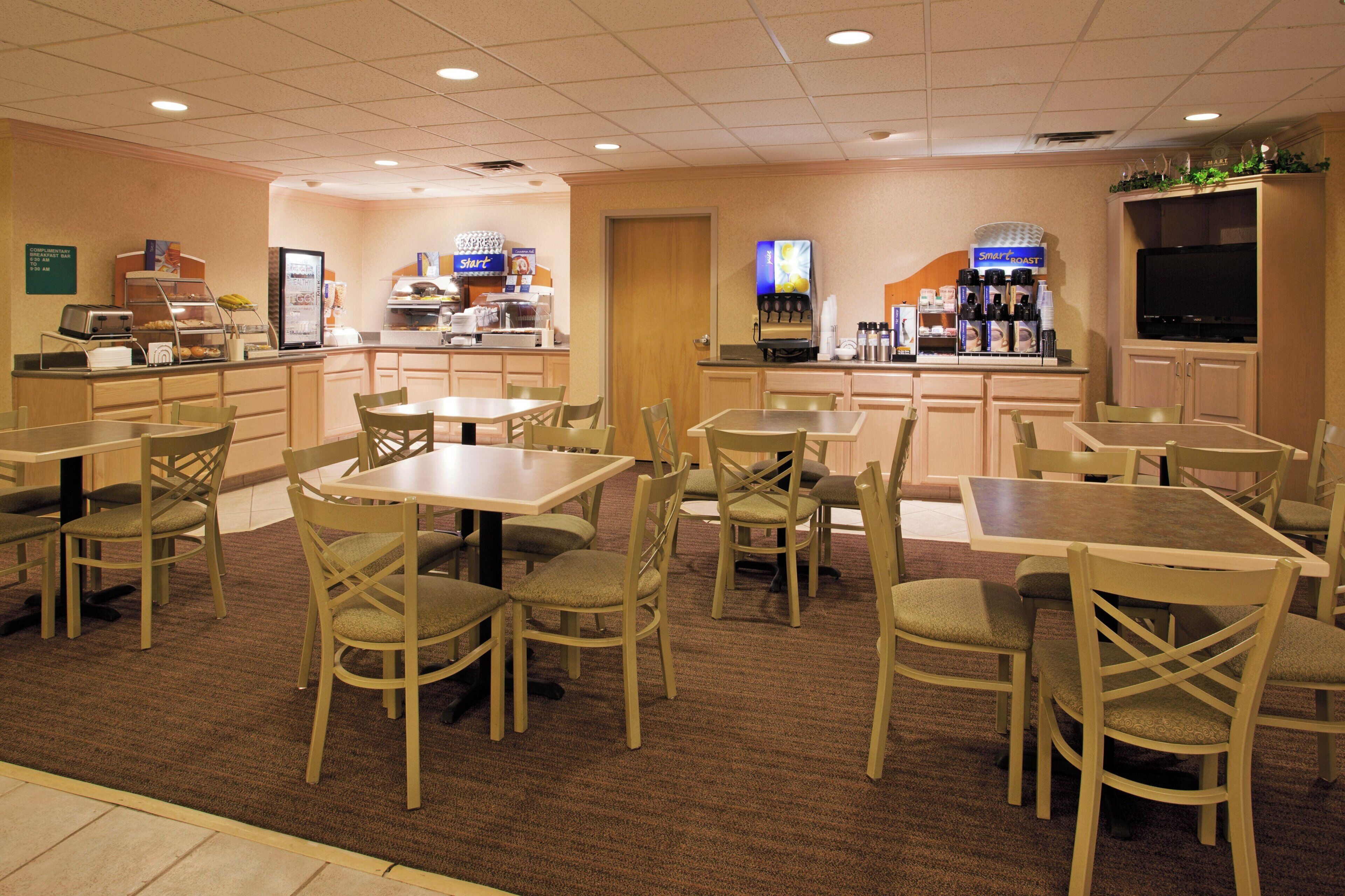 A hotel dining area with multiple tables and chairs, a coffee station, and a television.