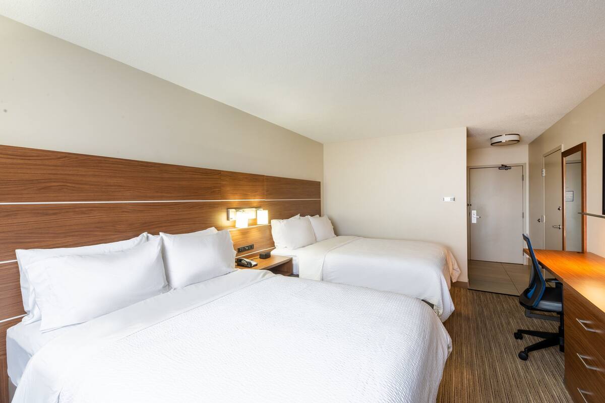 A hotel room with two beds, a desk, and a nightstand with a lamp.
