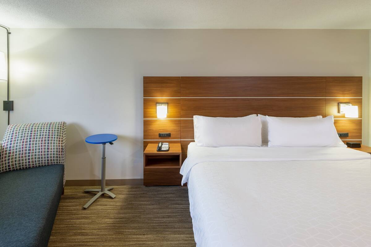 A hotel room with a large bed, a bedside table with a lamp, a small round table, and a chair.