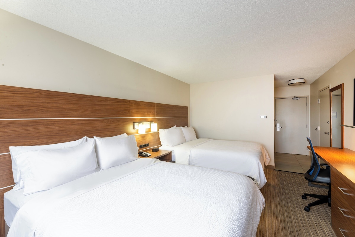 Une chambre d’hôtel avec deux lits, un bureau et une table de chevet avec une lampe.