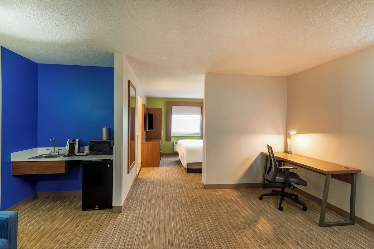 Une chambre d’hôtel équipée d’un bureau, d’une chaise, d’un lit et d’un petit coin cuisine.