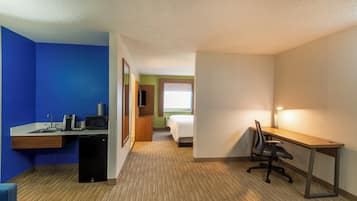 A hotel room with a desk, chair, bed, and a small kitchenette area.