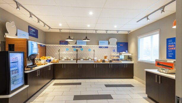 A modern kitchen area with a central island, various food stations, and a refrigerator on the left. - Holiday Inn Express Vermilion by IHG (Vermilion)