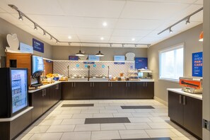 A modern kitchen area with a central island, various food stations, and a refrigerator on the left. - Holiday Inn Express Vermilion by IHG (Vermilion)
