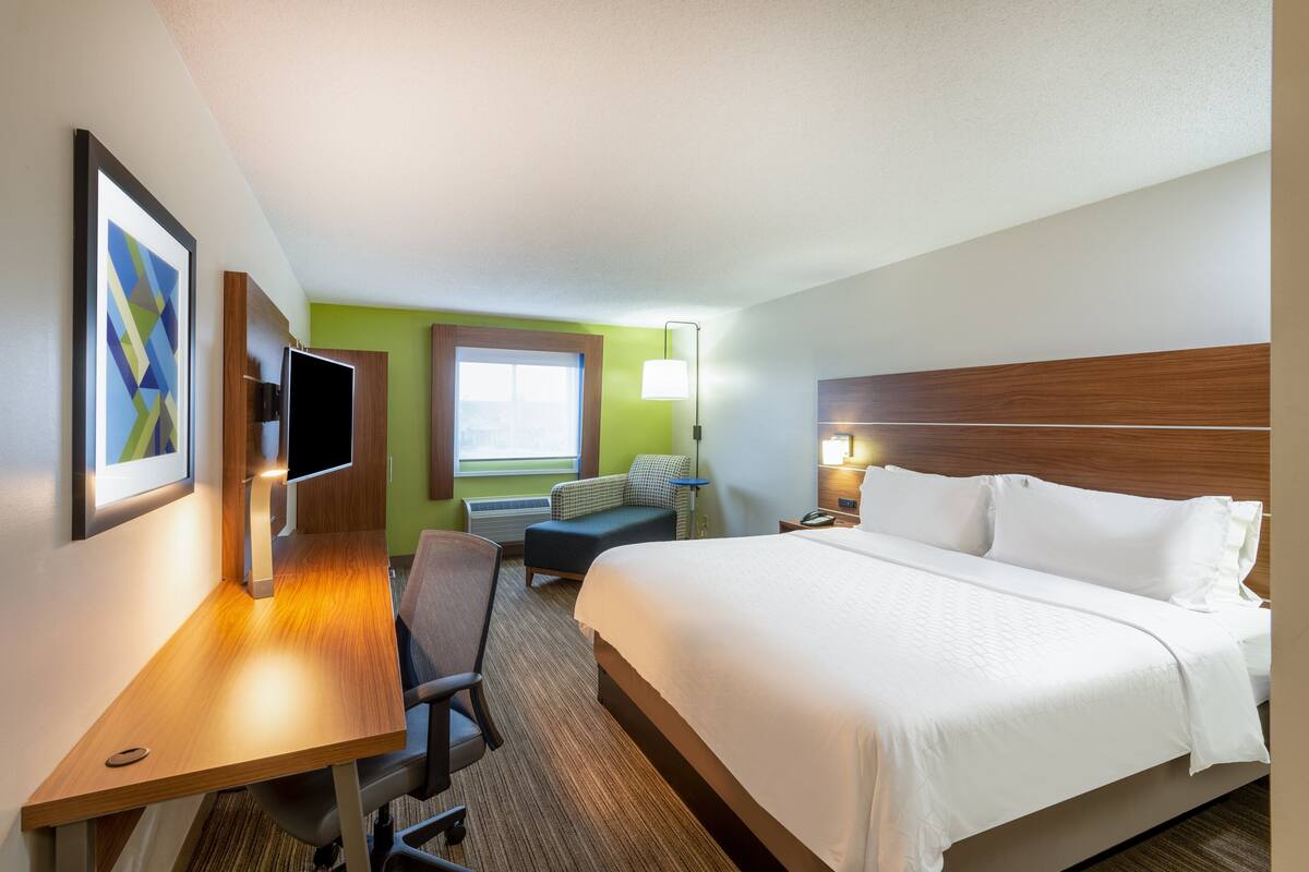 A hotel room with a bed, desk, chair, and a window with a view.