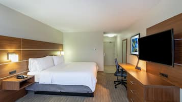 A hotel room with a bed, bedside table with a phone, a desk with a chair, a flat-screen TV, and a painting on the wall.