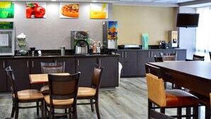 A modern hotel lobby with a coffee station, seating area, and a large screen.