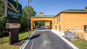 A Quality Inn sign, a welcome sign, and a building with a green roof and beige walls.
