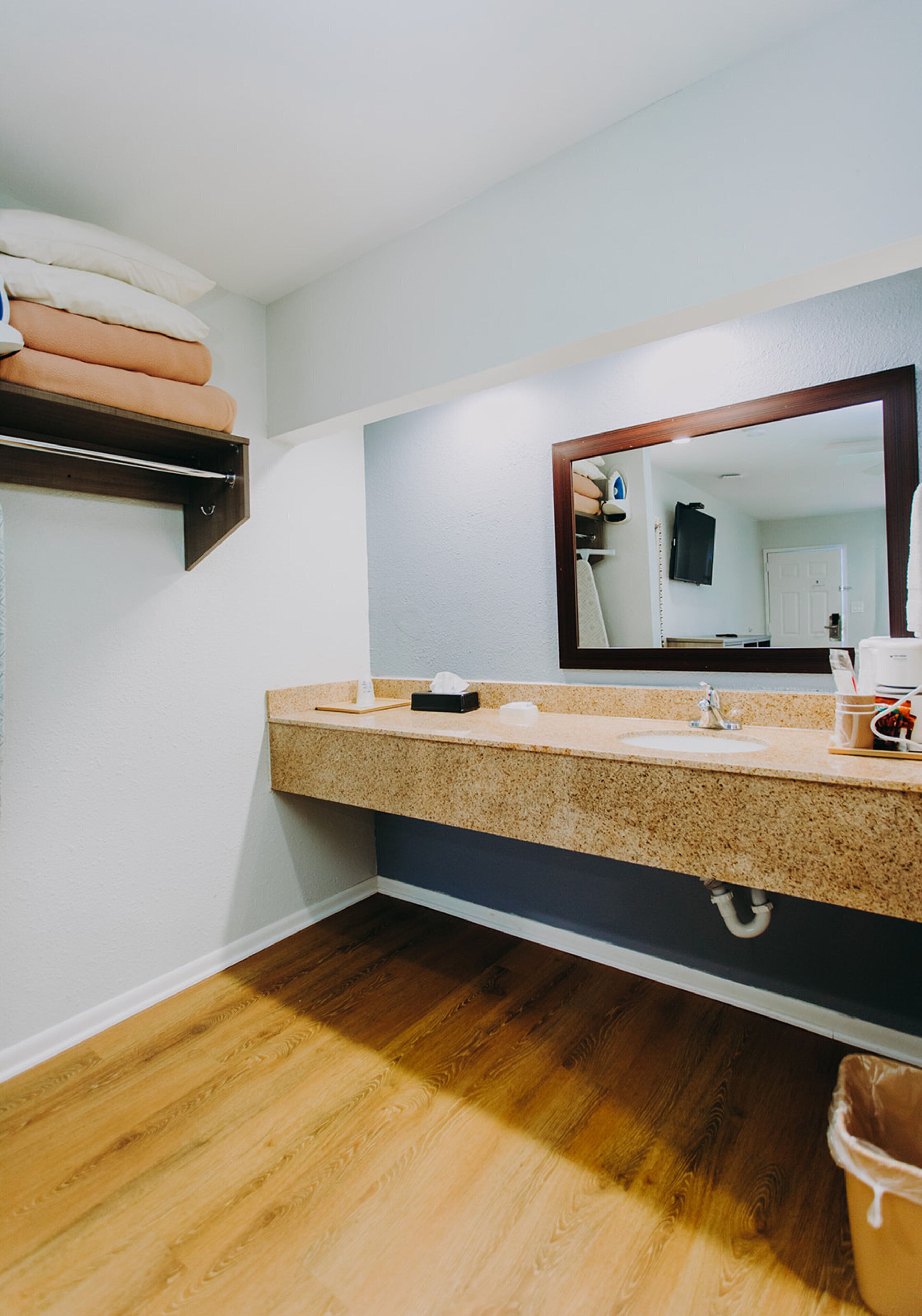A bathroom with a double sink, a mirror, a towel rack, and a wooden floor.