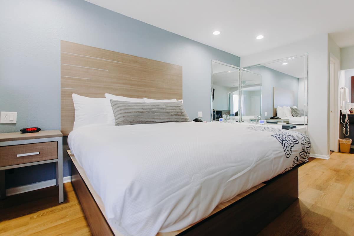 A modern hotel room with a large bed, bedside table, and a mirror.