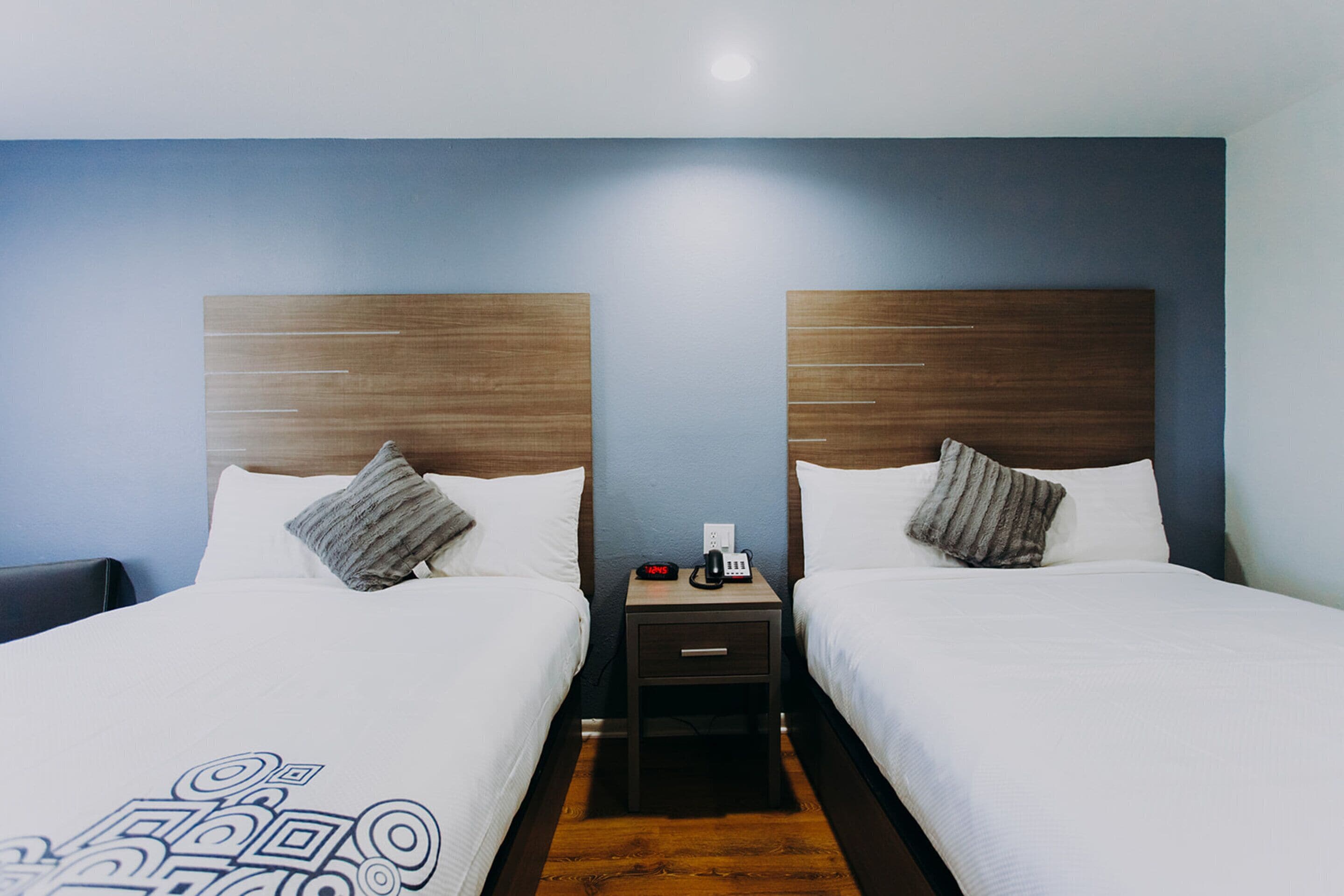 A hotel room with two beds, each with a wooden headboard, a bedside table, and a nightstand.