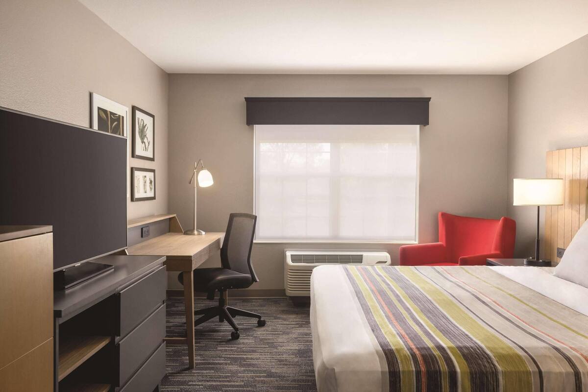 A hotel room with a bed, desk, chair, and a window with blinds.