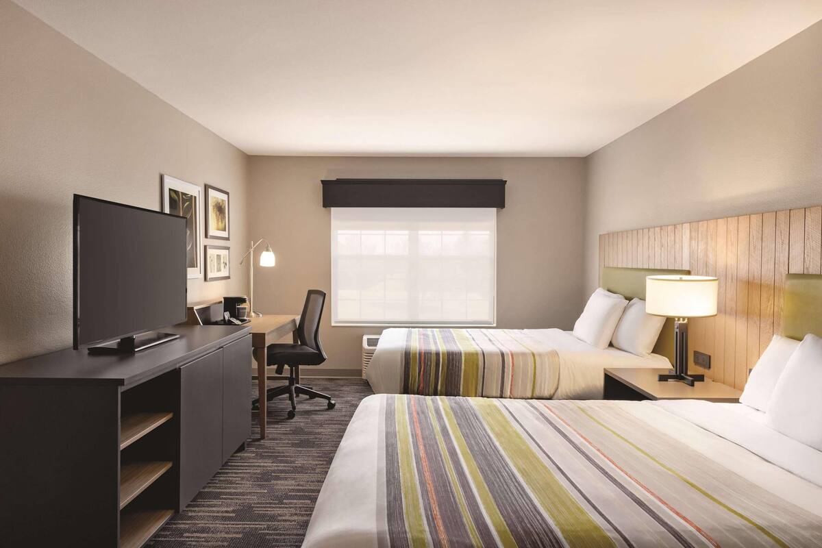 A hotel room with two beds, a TV, a desk, and a lamp.