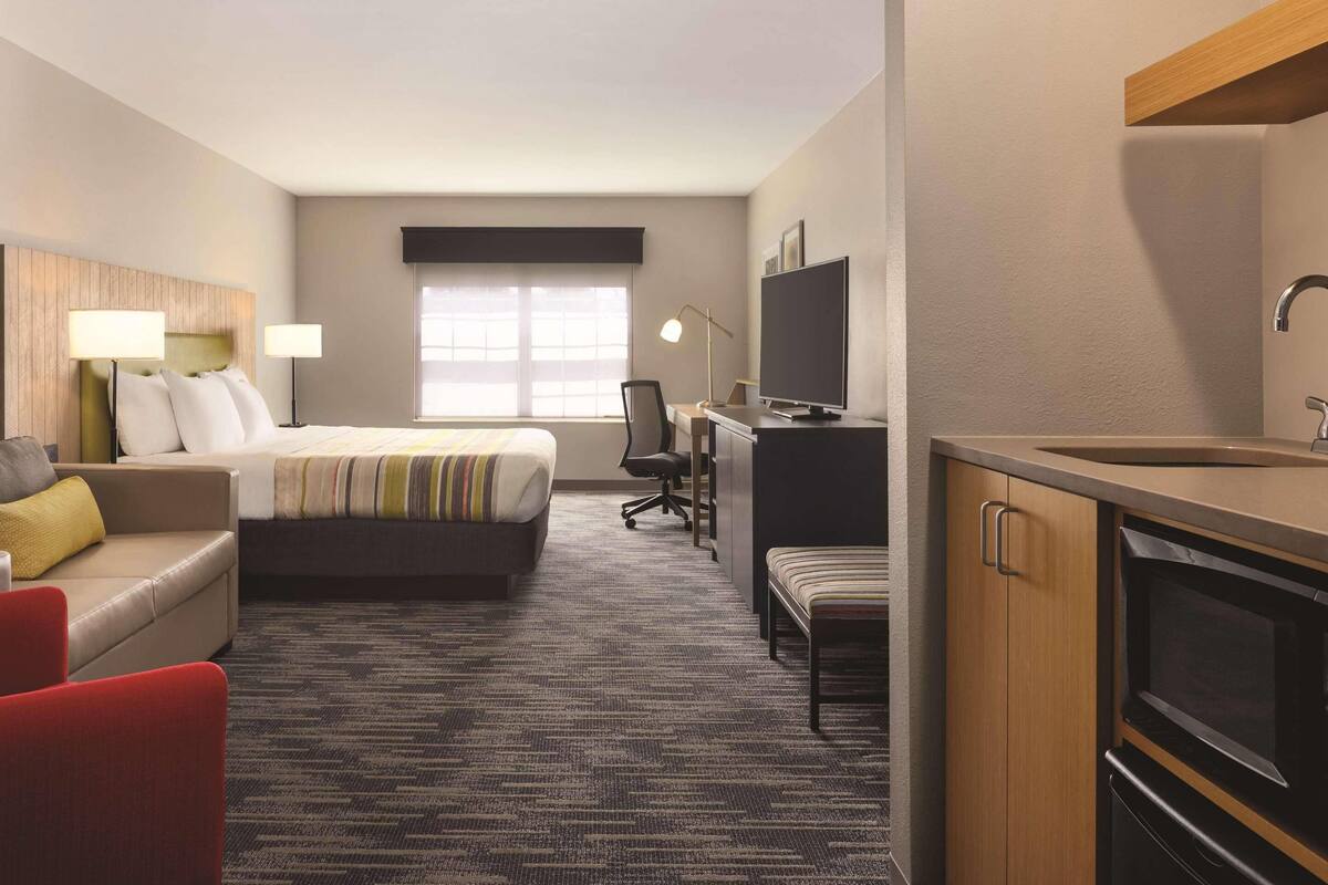 A hotel room with a bed, a desk, a TV, a kitchenette, and a window.