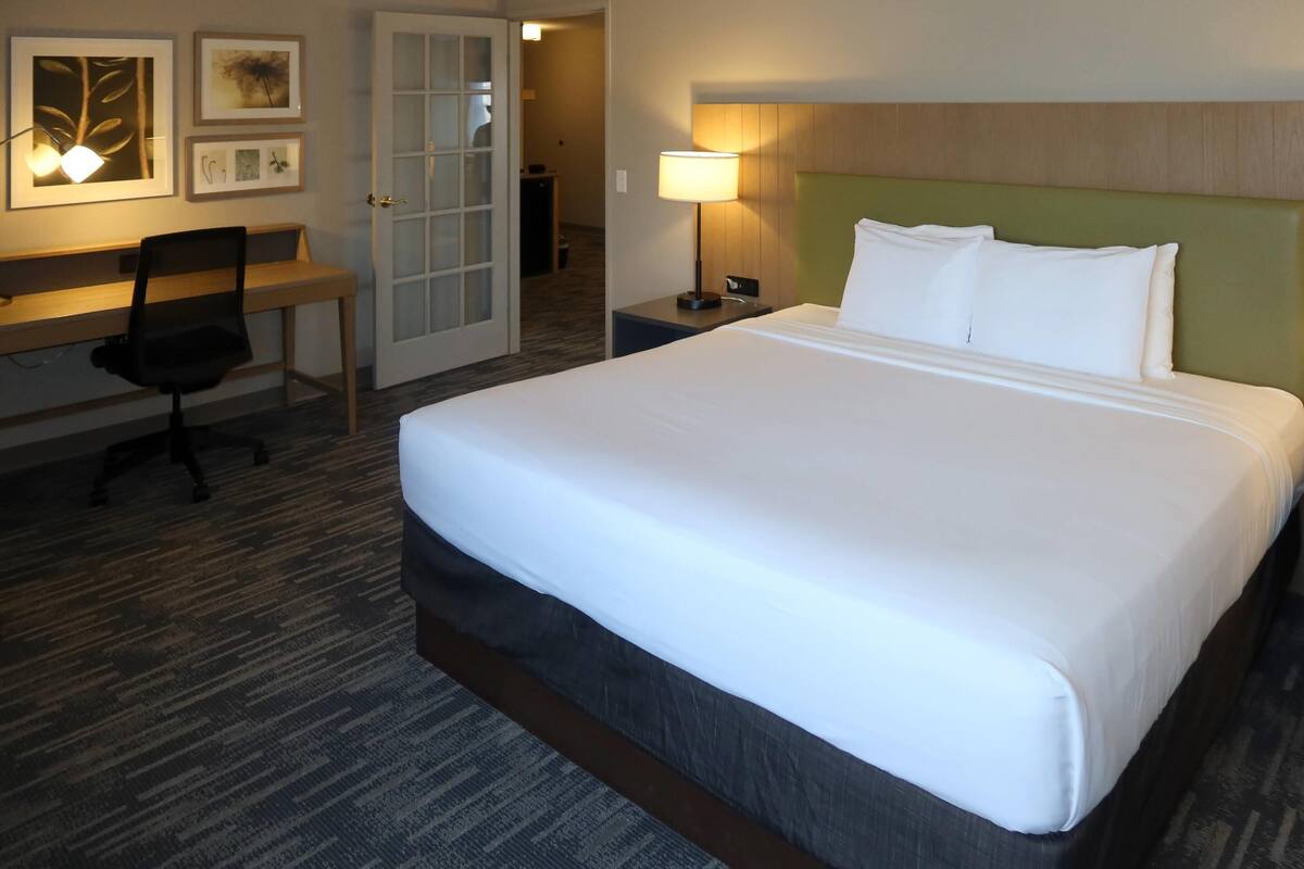 A hotel room with a large bed, a desk, a chair, and a lamp.