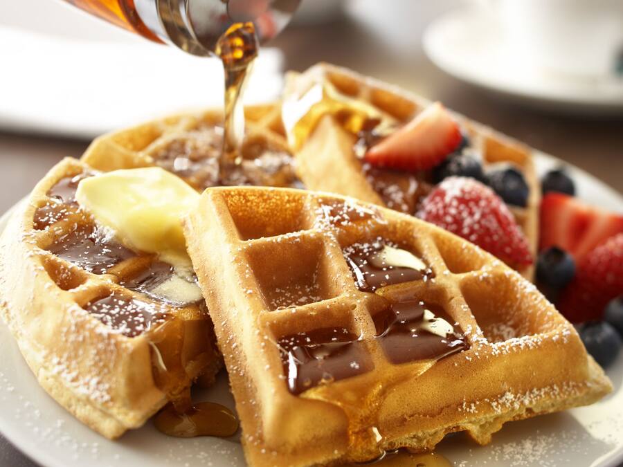 Ein Teller mit Waffeln, Sirup, Butter und Obst.