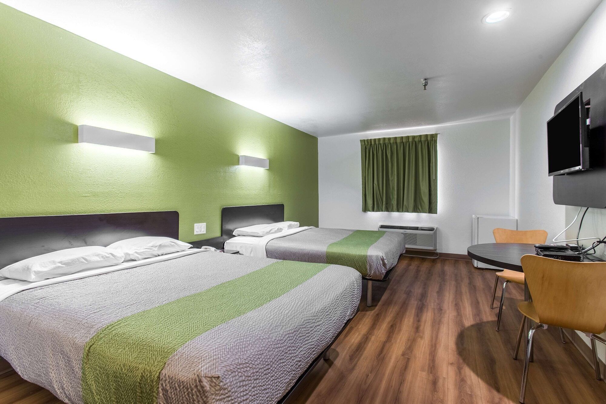 Una habitación de hotel con dos camas, un escritorio, una silla, un televisor y una ventana con cortinas.