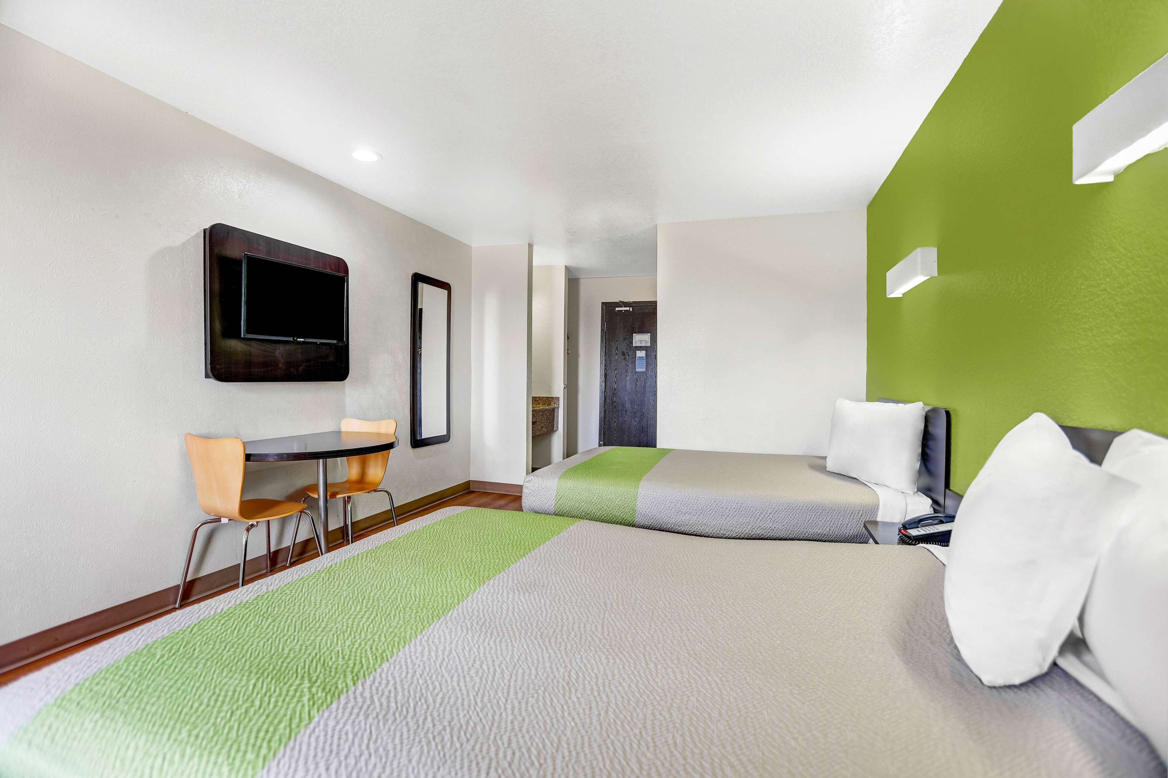 Habitación de hotel con dos camas, un escritorio, una silla, un televisor y una pared de acento verde.