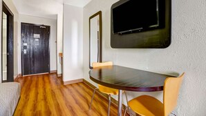 A room with a wooden floor, a round table with two yellow chairs, a flat-screen TV mounted on the wall, and a dark wooden door. - Motel 6 Moriarty, NM (Moriarty)