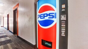 A hallway with a vending machine featuring Pepsi branding, a carpeted floor, and doors along the corridor. - Motel 6 Moriarty, NM (Moriarty)