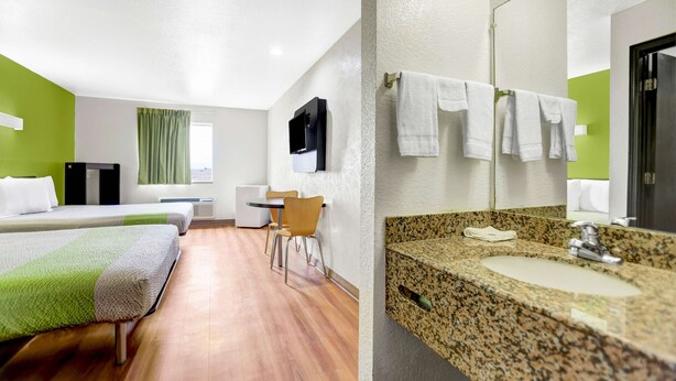 A hotel room with two beds, a desk, a chair, a television, and a bathroom with a sink and towel rack. - Motel 6 Moriarty, NM (Moriarty)