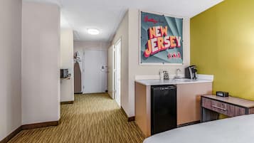 Una habitació d'hotel amb un llit, una petita taula de nit amb un rentanet, un mirall i un cartell a la paret.