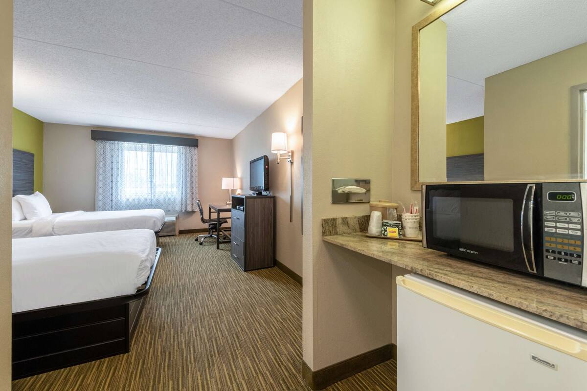 Una habitación de hotel con dos camas, un escritorio, un televisor, un microondas y un refrigerador.