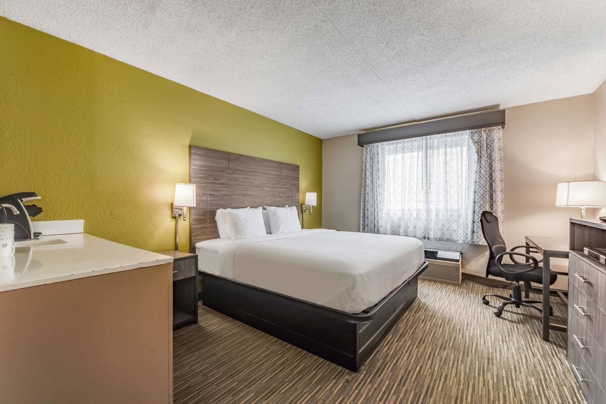 Una habitación de hotel con cama, escritorio, silla y ventana con cortinas.