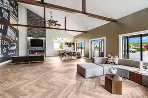 A spacious living area with a herringbone wood floor, a large sofa, a coffee table, and a fireplace. There is a dining area with a table and chairs, and a kitchen in the background. - SureStay Plus Hotel by Best Western McGuire AFB Jackson (Cookstown)