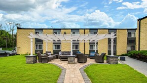 A covered outdoor seating area with a stone pathway leading to it, surrounded by a well-maintained lawn and a building with multiple windows. - SureStay Plus Hotel by Best Western McGuire AFB Jackson (Cookstown)