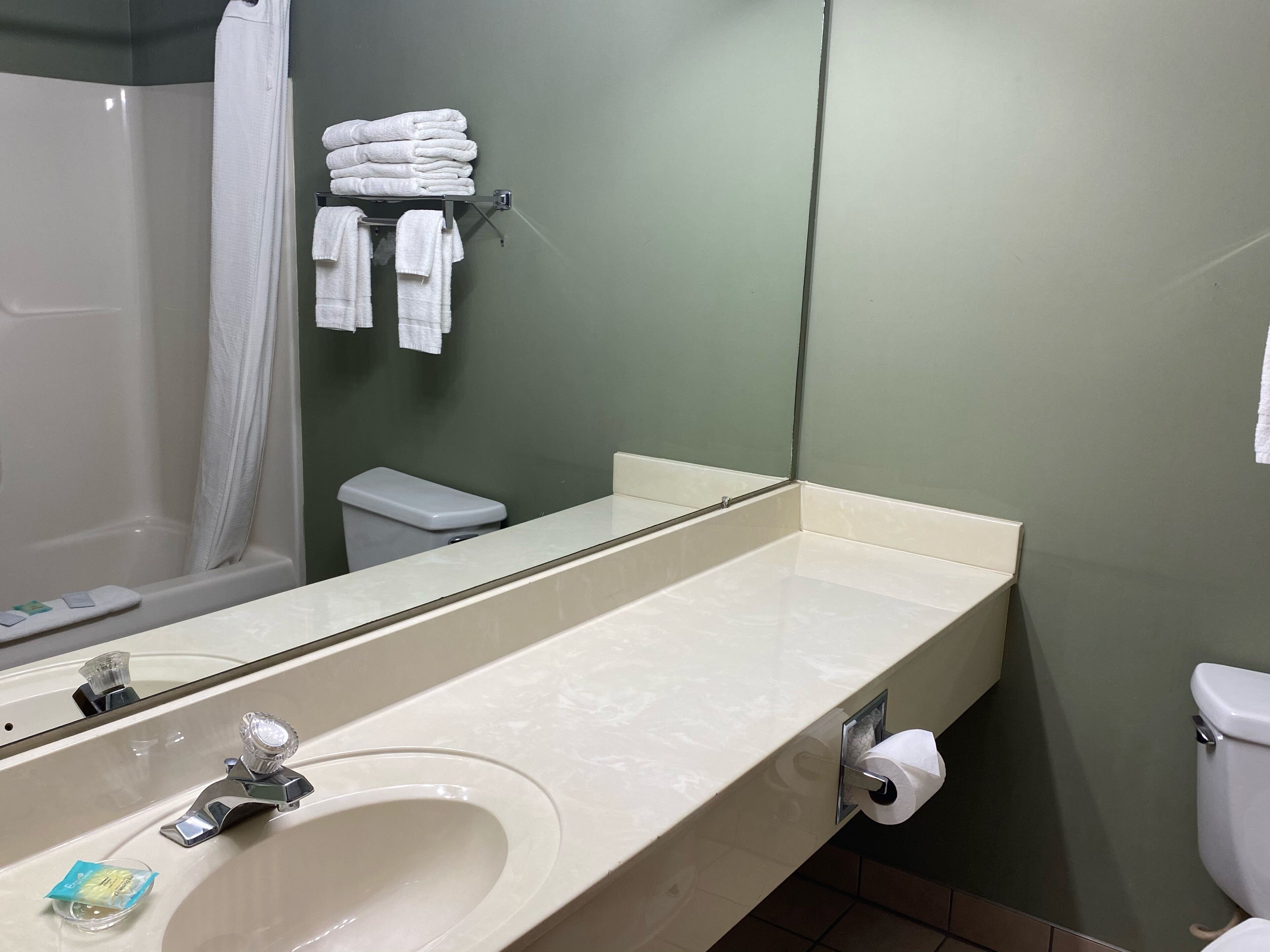 A bathroom with a sink, mirror, toilet, and a stack of towels on a rack.
