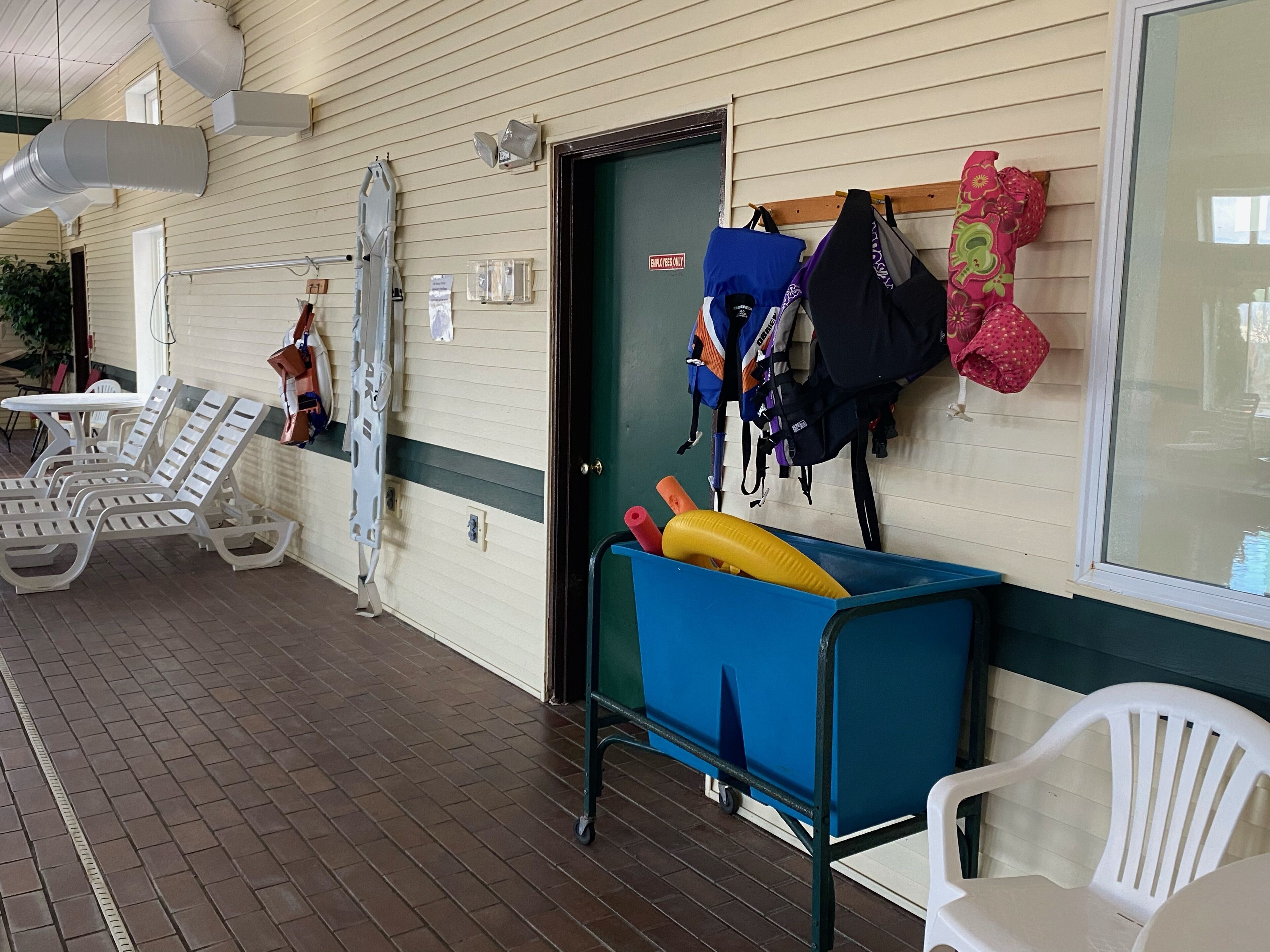 A covered outdoor area with lounge chairs, a blue cart with items, and a wall-mounted rack with bags.