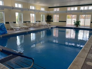 An indoor swimming pool with clear water, a diving board, and lounge chairs.