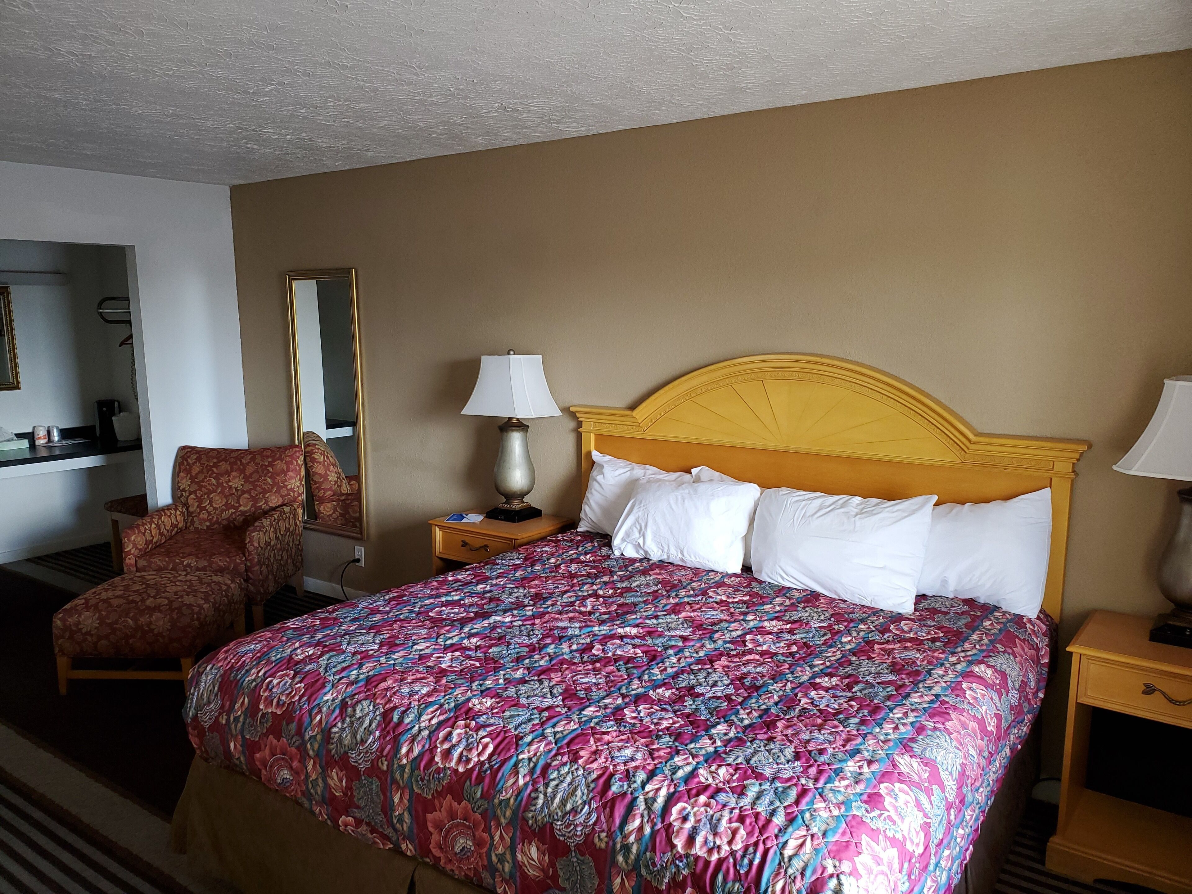 A hotel room with a large bed, a chair, a nightstand with a lamp, and a mirror on the wall.