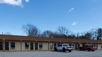 A motel with a row of single-story rooms, a parking lot, and a clear sky.