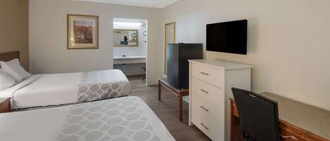 A hotel room with two beds, a desk, a TV, a dresser, and a mirror.