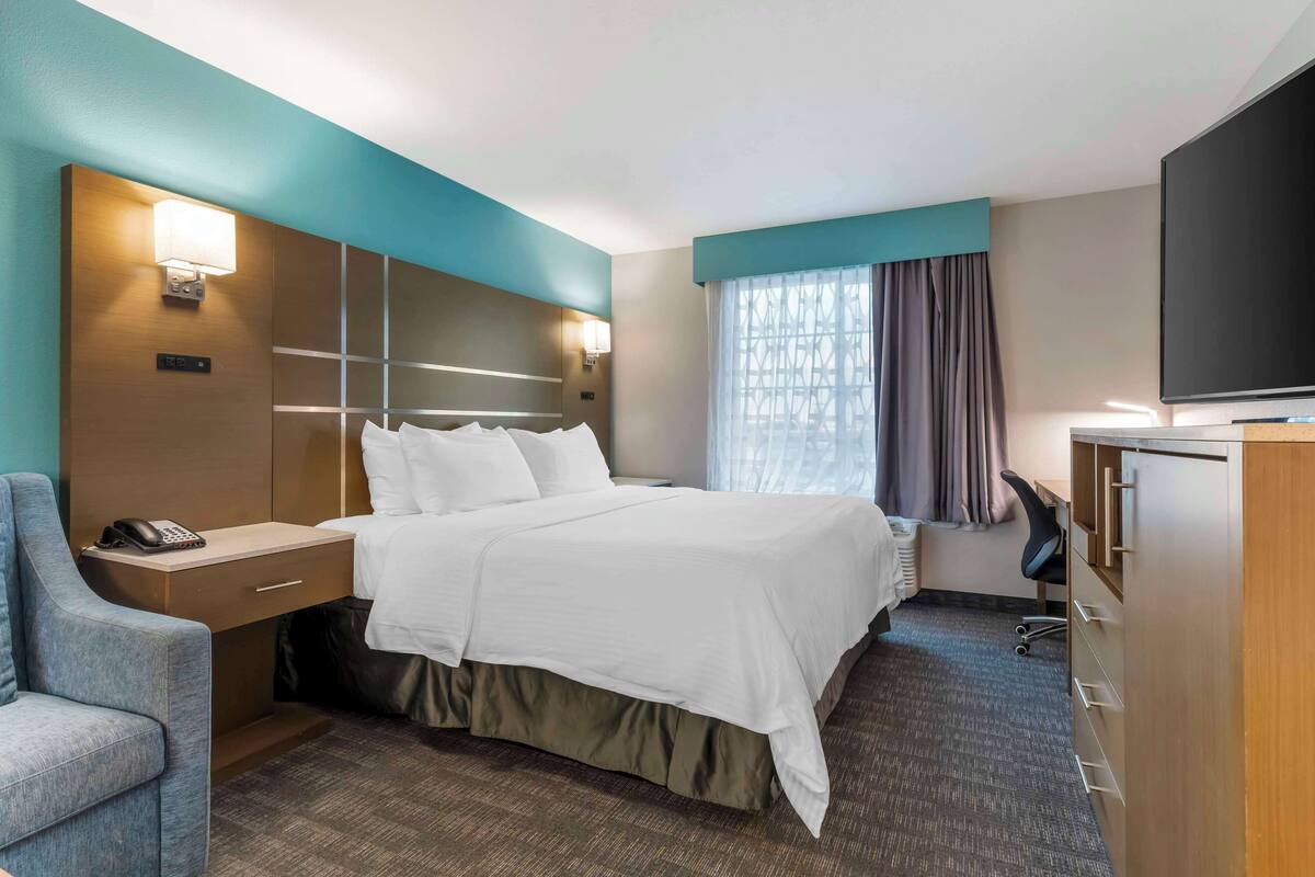 A hotel room with a bed, a desk with a telephone, a chair, a TV, and a wardrobe.
