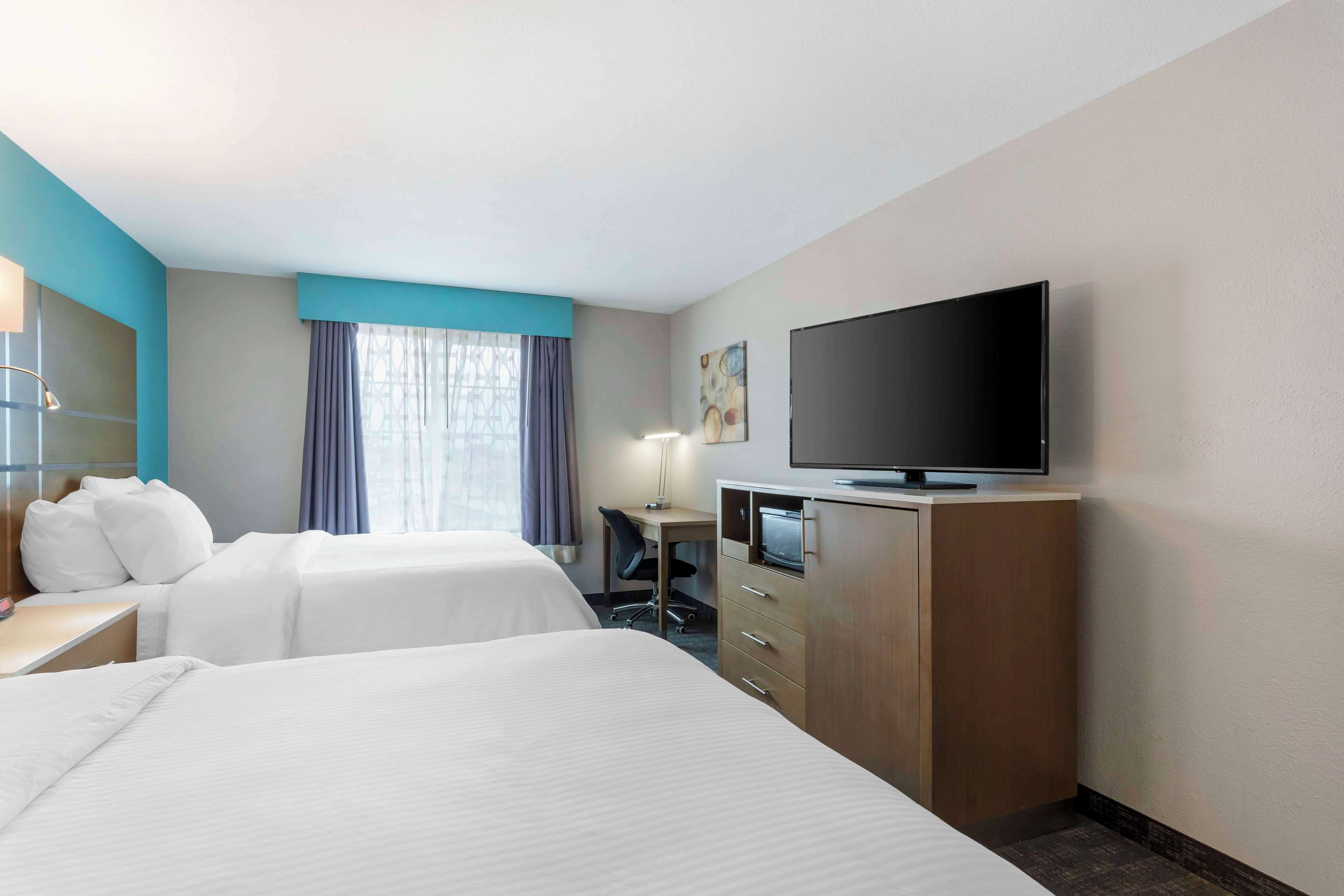 A hotel room with two beds, a desk, a TV, and a window with curtains.