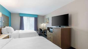 Habitación de hotel con dos camas, un escritorio, un televisor y una ventana con cortinas.