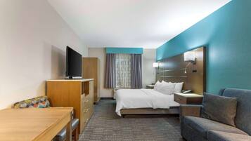 Una habitación de hotel con cama, escritorio, televisor, sofá y mesita de noche.