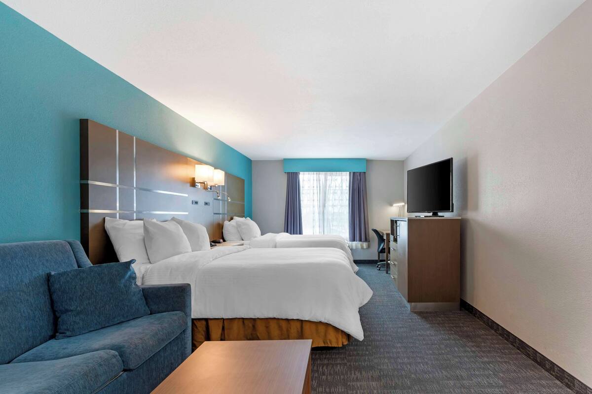A hotel room with a bed, two bedside tables, a TV, a sofa, and a desk.