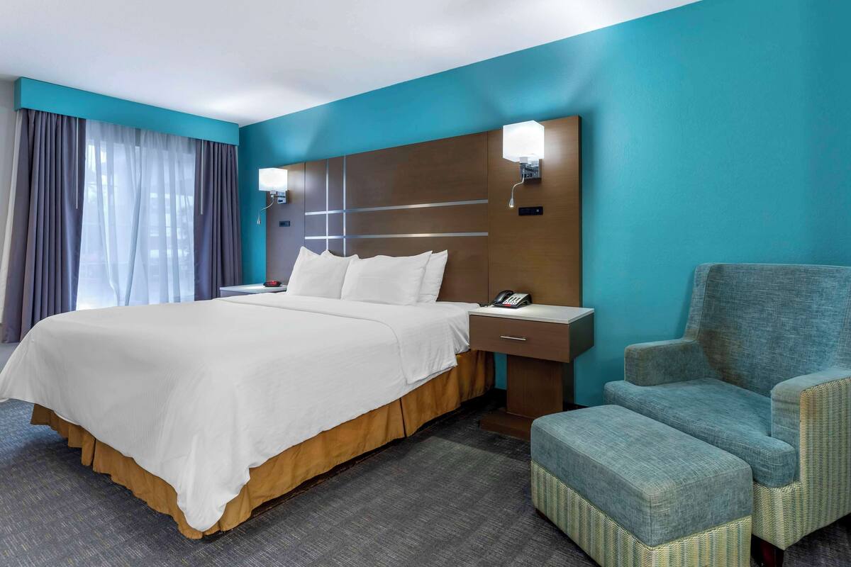 A hotel room with a large bed, a nightstand, a chair, and a desk.