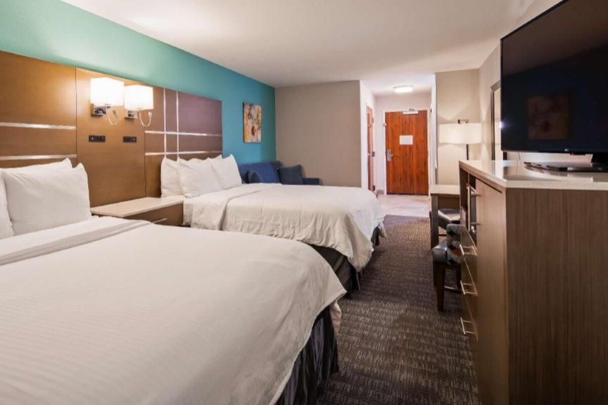 A hotel room with two beds, a desk, a TV, and a bathroom visible in the background.