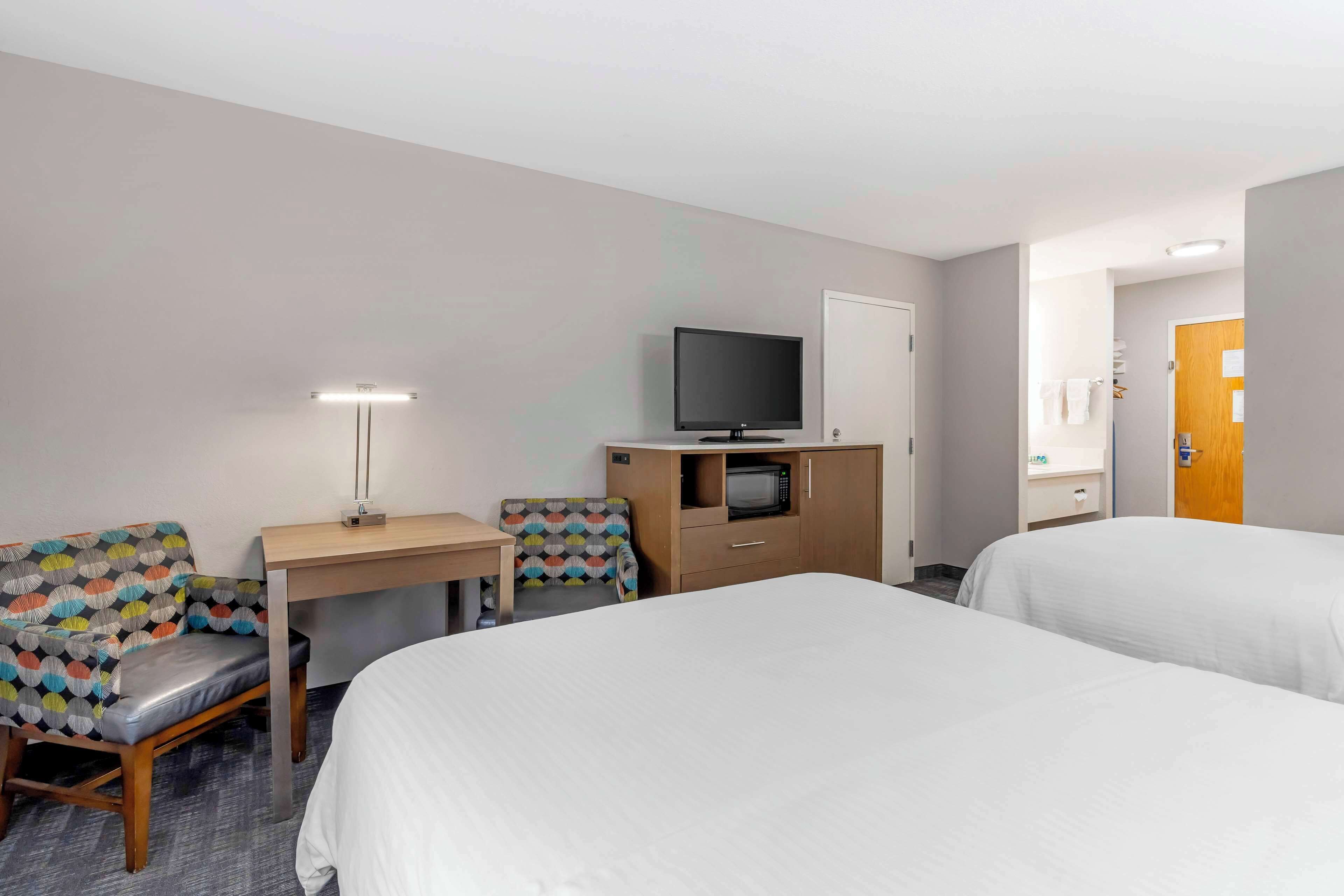 A hotel room with two beds, a desk with a television, a microwave, and a lamp.