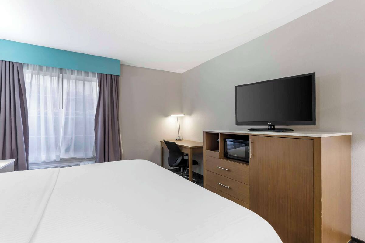A hotel room with a large bed, a desk with a chair, a television on a wooden cabinet, and a window with curtains.